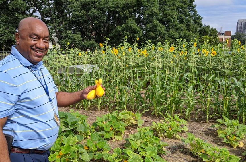 a man standing on the rooftop garden displaying a squash that was grown there