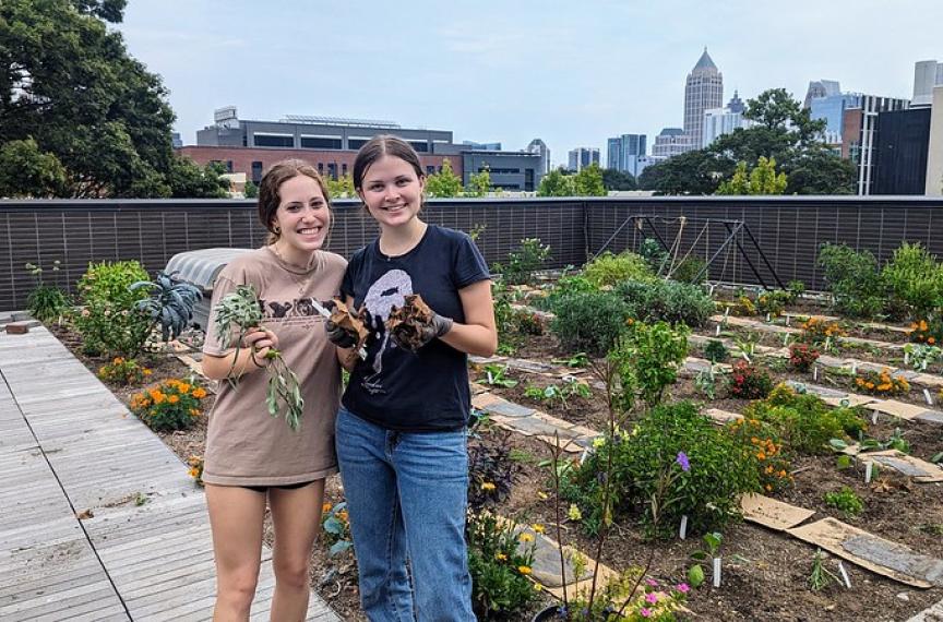 two students showing vegetables while standing on the rooftop garden